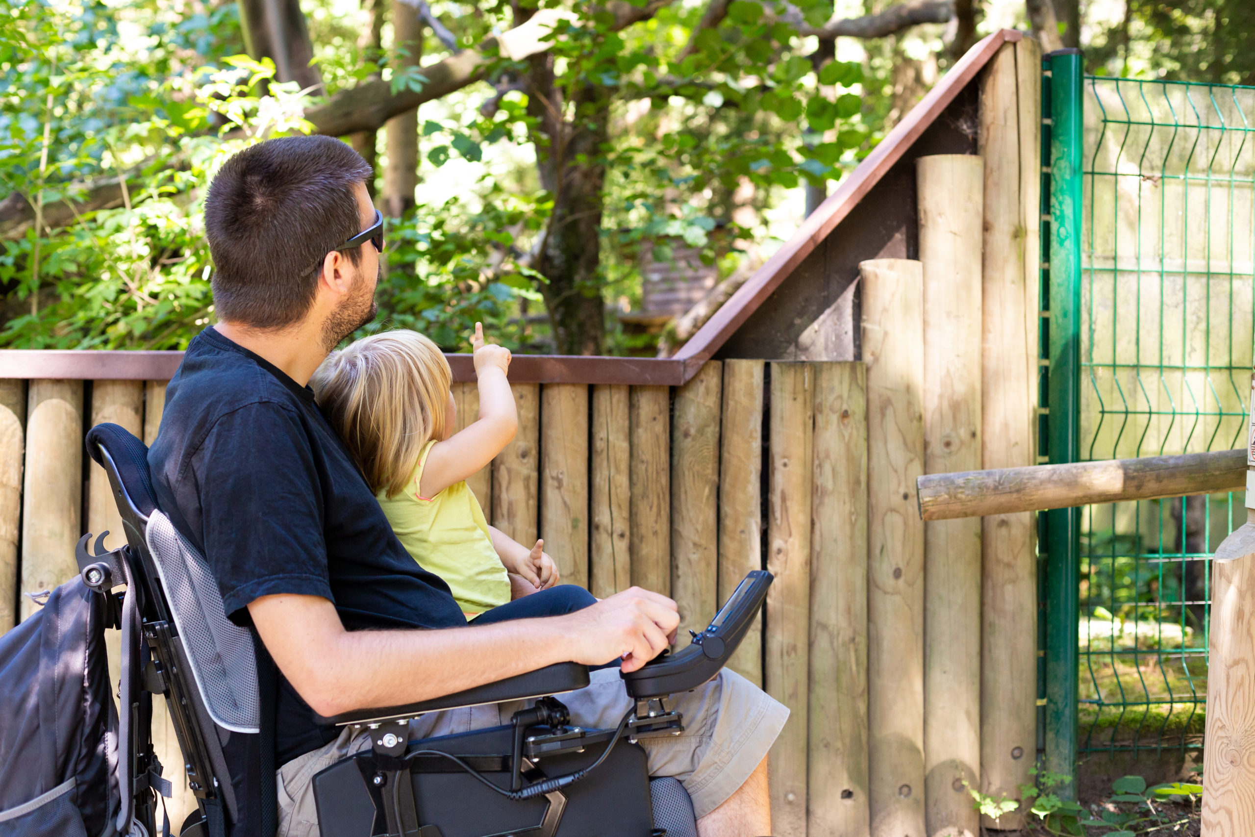 Disabled Father in Wheelchair enjoying Nature with Daughter Girl in Outside zoo park on a sunny day.