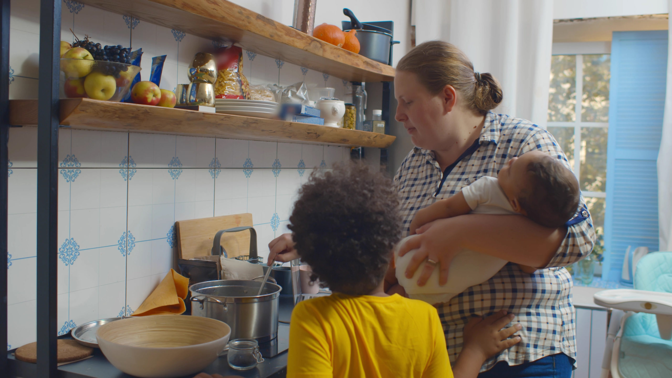 Woman housewife holding sleeping infant and cooking dinner in kitchen talking to older children. Babysitter rocking newborn and preparing meal for preschool kid in kitchen