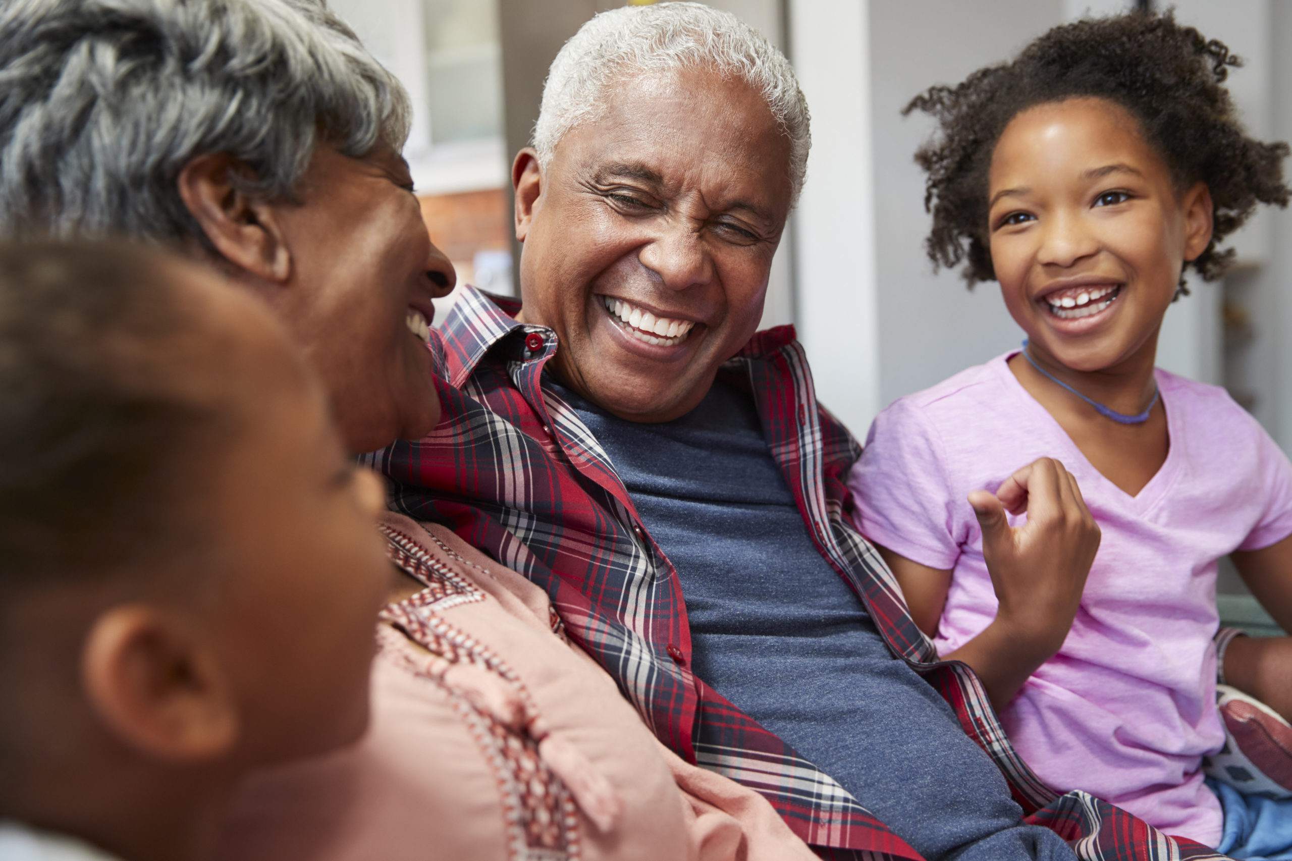 Grandparents Relaxing On Sofa At Home With Granddaughters