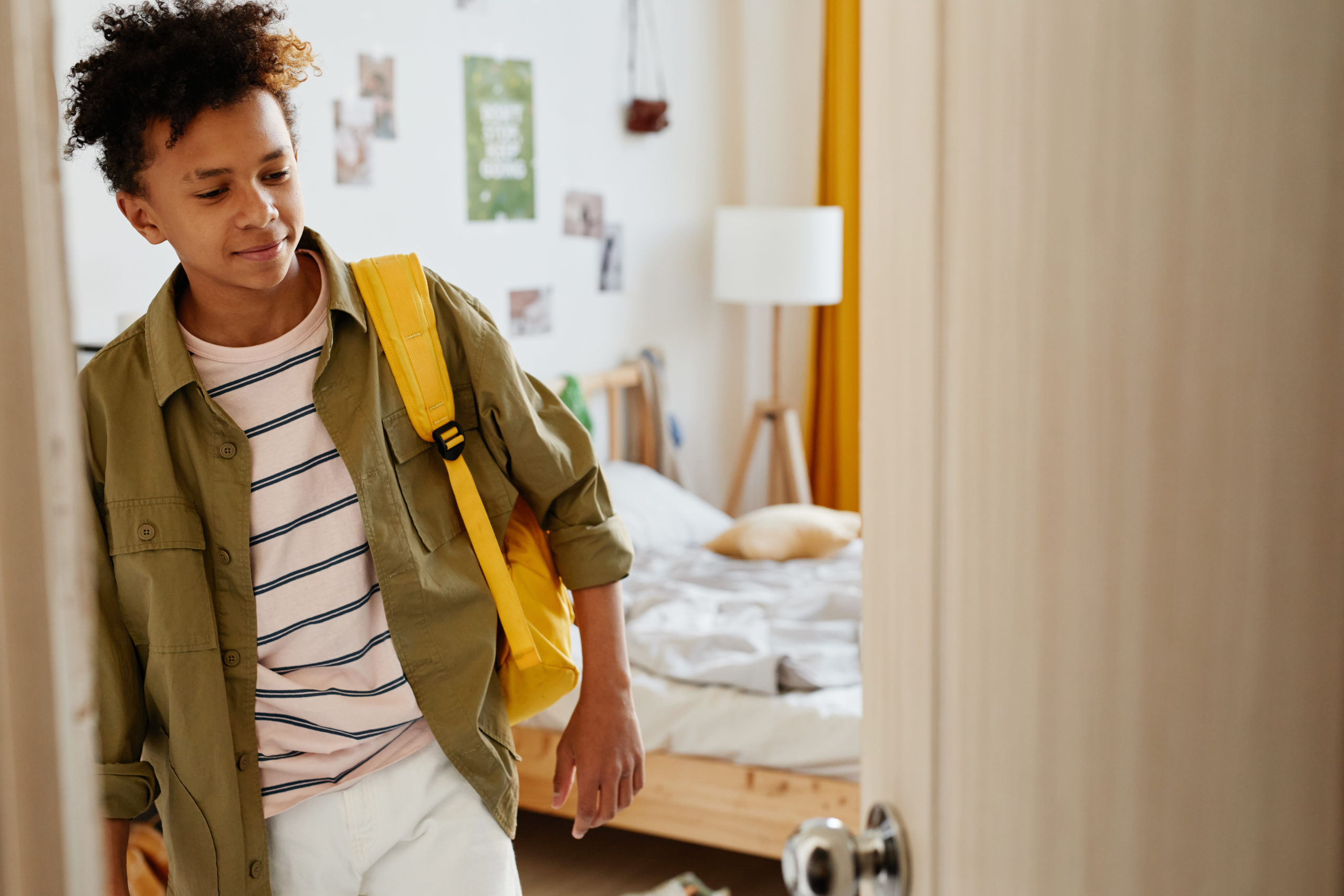 Waist up portrait of mixed-race teenage boy holding backpack and opening door while leaving for school in morning, copy space