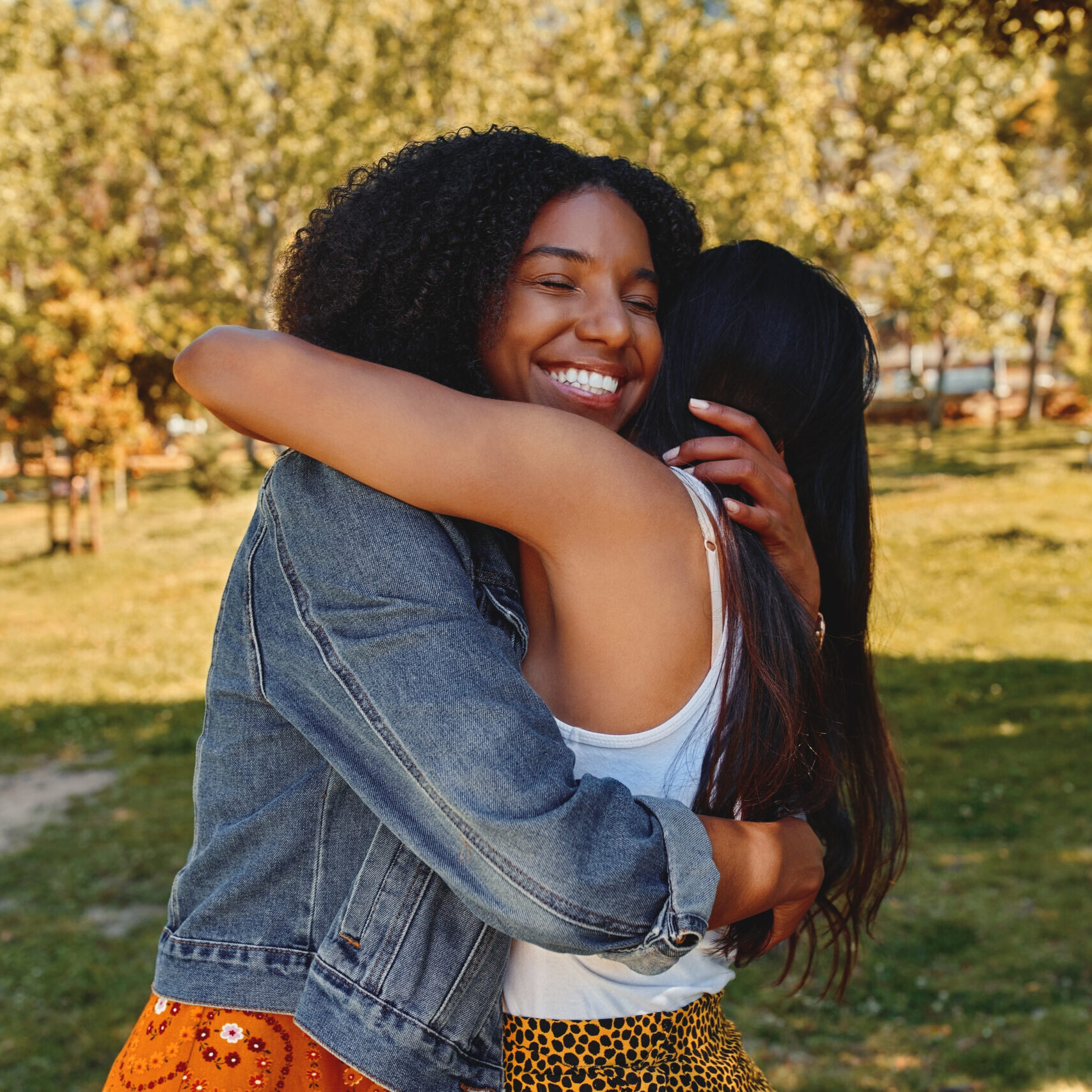 Two happy affectionate diverse young women friends hugging each other in the park - two friends hugging each other outdoors Two happy diverse female friends hugging in the park on a sunny day